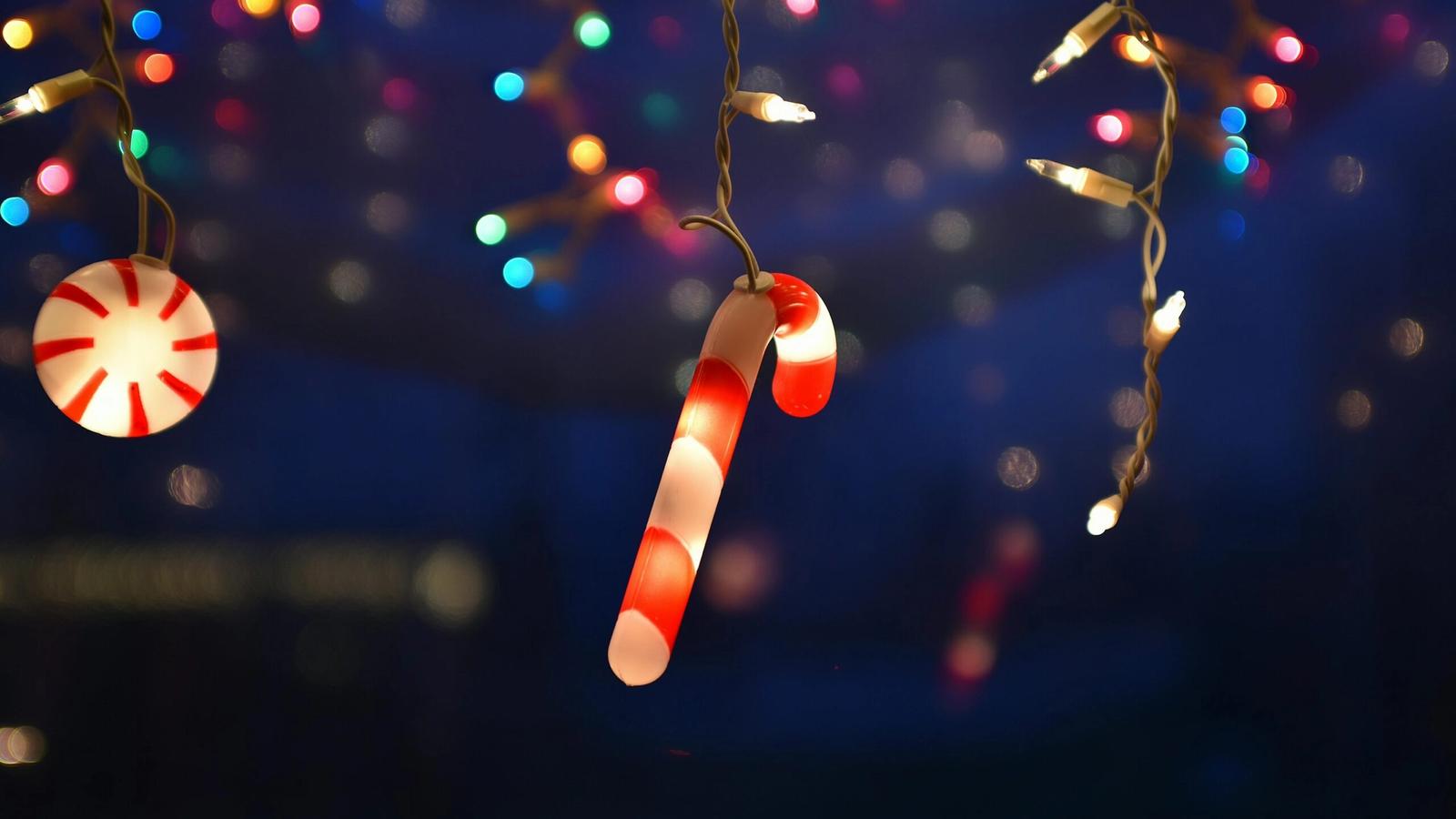 A glowing candy cane and peppermint light hang among multicolored string lights, creating a festive holiday atmosphere reminiscent of the best Christmas lights in Gatlinburg TN against a dark, blurry background.