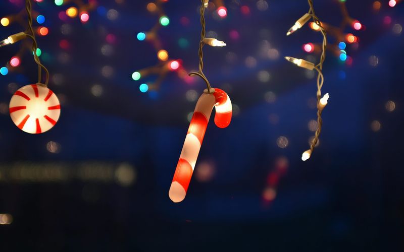 A glowing candy cane and peppermint light hang among multicolored string lights, creating a festive holiday atmosphere reminiscent of the best Christmas lights in Gatlinburg TN against a dark, blurry background.