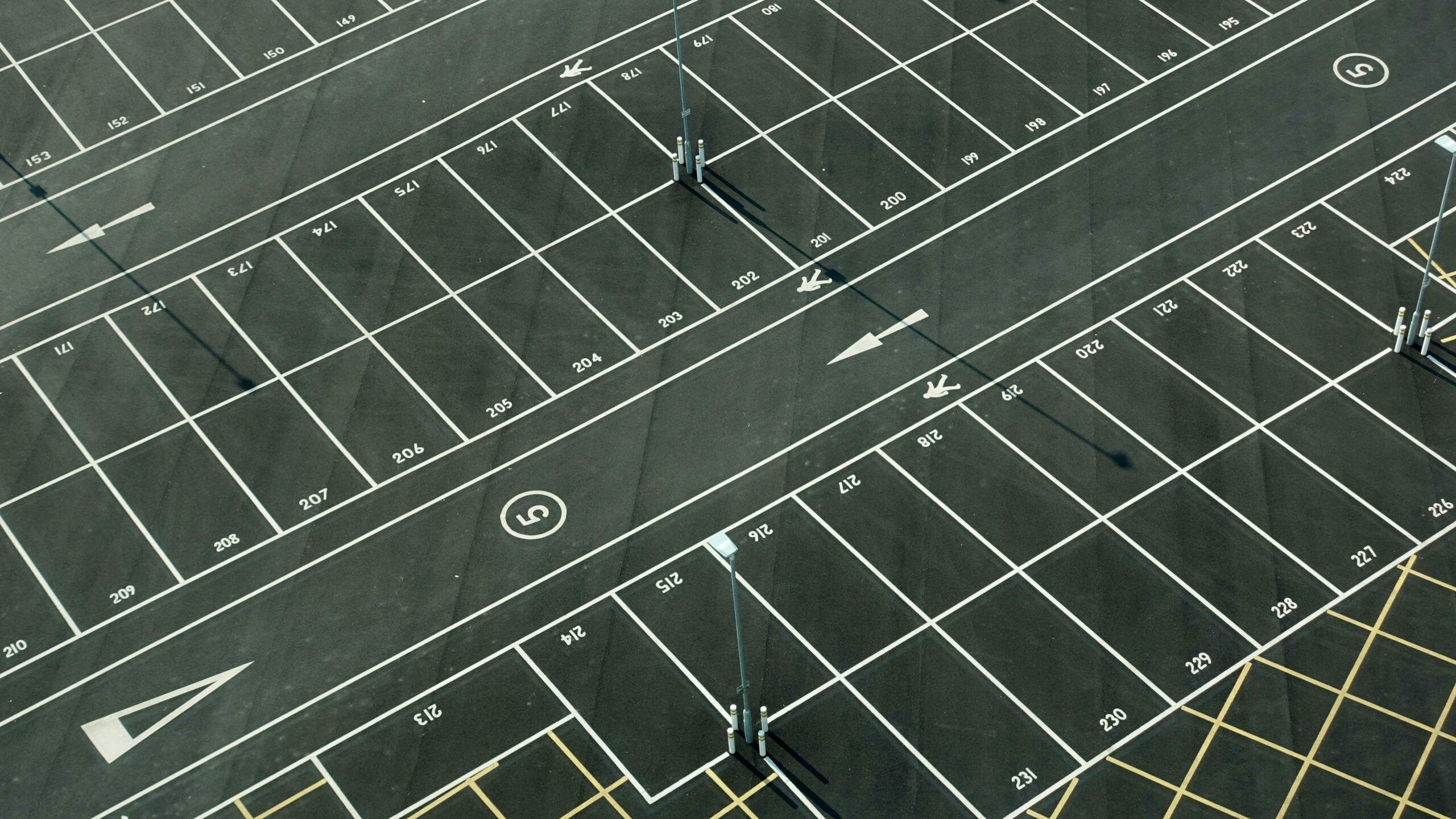 Aerial view of an empty, freshly painted parking lot with white-lined spaces, numbers on each space, arrows indicating directions, and several light poles casting long shadows—ideal for anyone seeking free parking near Gatlinburg parking garages.