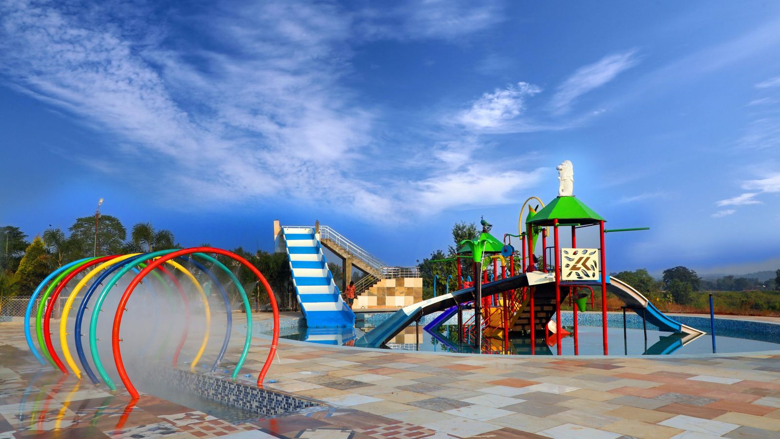 A colorful outdoor water playground at Soaky Mountain Waterpark features slides, climbing structures, and water spray arches under a bright blue sky, with tiled flooring and greenery—perfect for any travel guide.