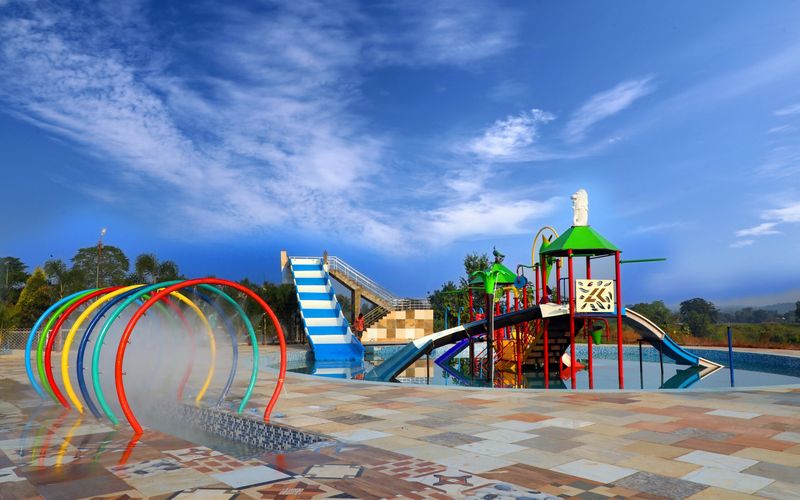 A colorful outdoor water playground at Soaky Mountain Waterpark features slides, climbing structures, and water spray arches under a bright blue sky, with tiled flooring and greenery—perfect for any travel guide.