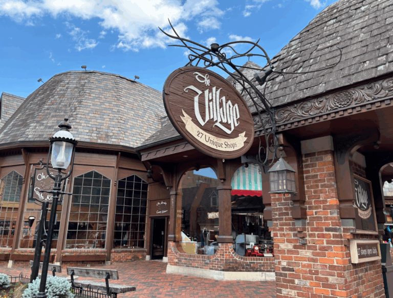 A rustic brick and wood building with a sign reading “The Village: 27 Unique Shops.” The curved shingle roofs and large windows evoke old-world charm, making the Village Shops Gatlinburg a must-see for memorable Gatlinburg shopping.