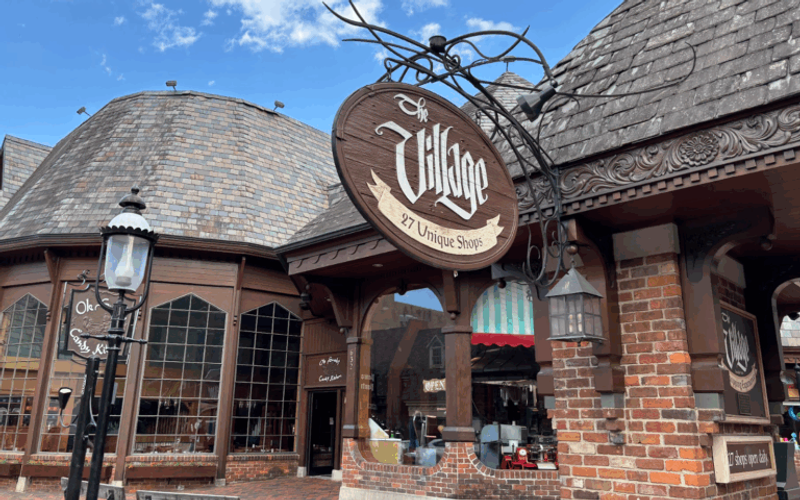 A rustic brick and wood building with a sign reading “The Village: 27 Unique Shops.” The curved shingle roofs and large windows evoke old-world charm, making the Village Shops Gatlinburg a must-see for memorable Gatlinburg shopping.
