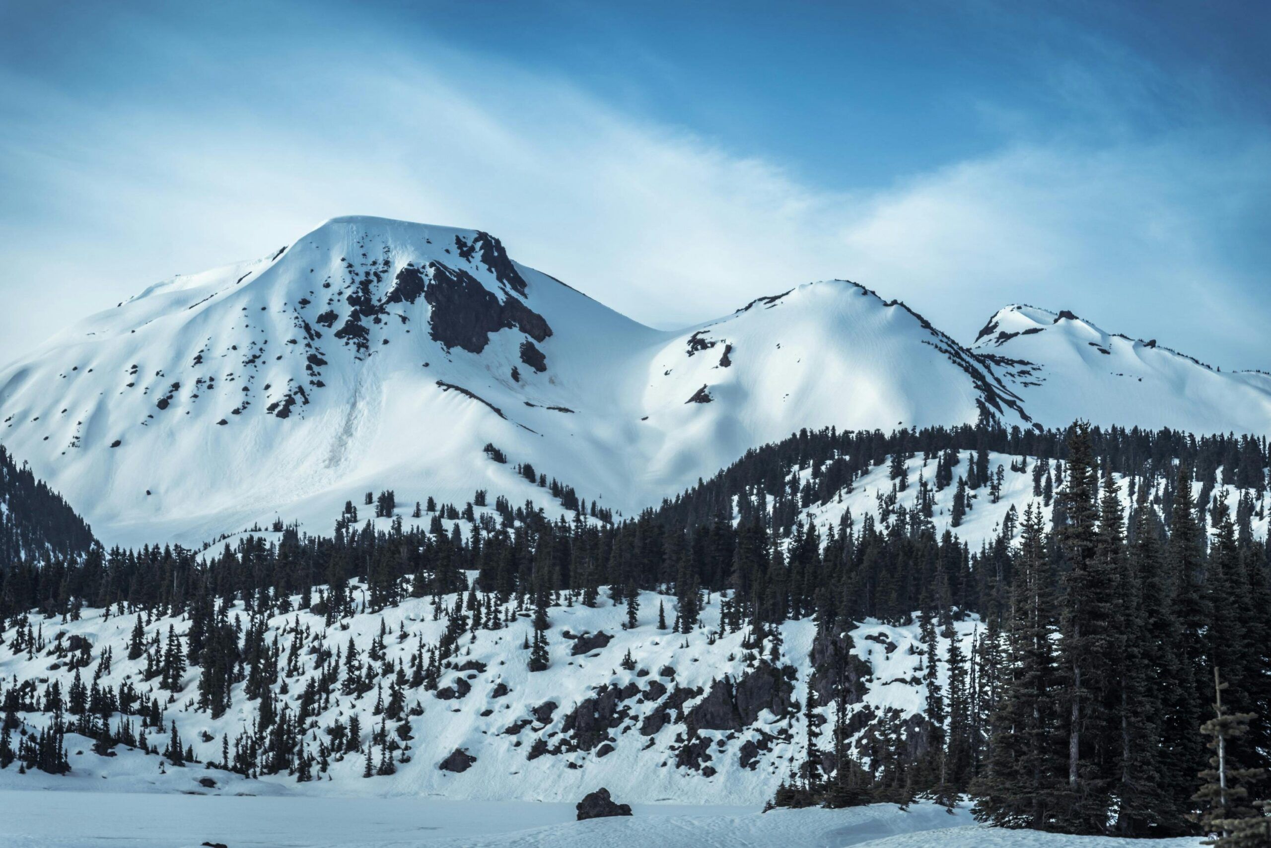 Snow-covered mountain peaks rise under a blue sky, with dark pine trees covering the lower slopes and patches of exposed rock—one of the many stunning sights to enjoy among the things to do in Gatlinburg in winter.