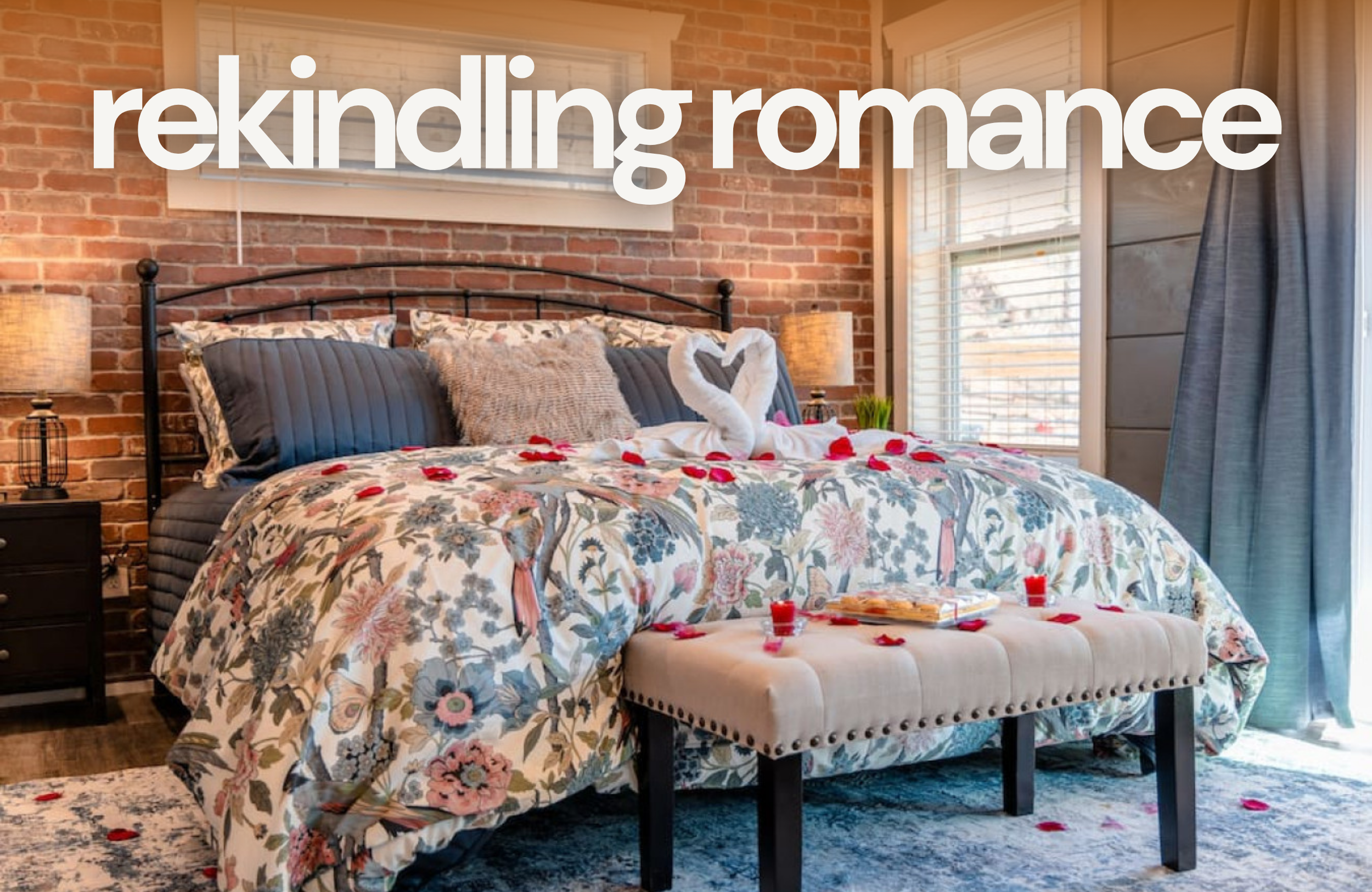 A cozy bedroom with a floral bedspread, swan towels, and rose petals on the bed sets the scene for a couples retreat. Warm lighting and brick walls create a romantic atmosphere, with "rekindling romance" in large white text above.
