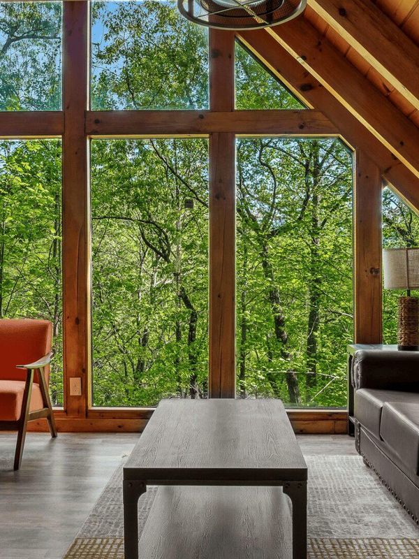 A living area with a sofa and two chairs, with large windows in the background.