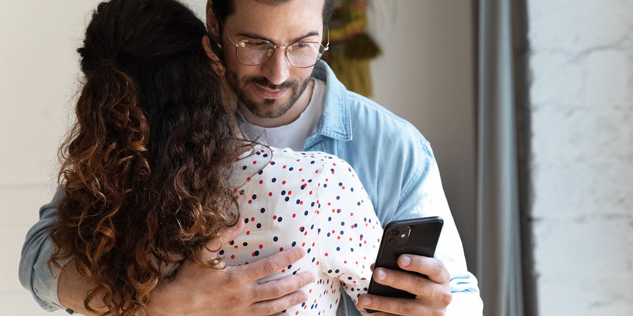 A couple in a warm embrace; one appears distracted by their phone, indicating possible infidelity.
