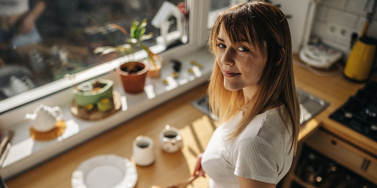 A woman happy in her kitchen, making herself some food.