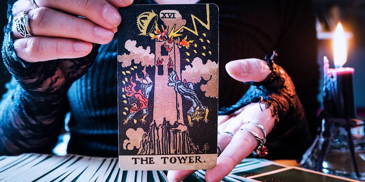 A psychic holding The Tower tarot card beside candlelight, symbolising sudden upheaval, revelations, and powerful transformation.