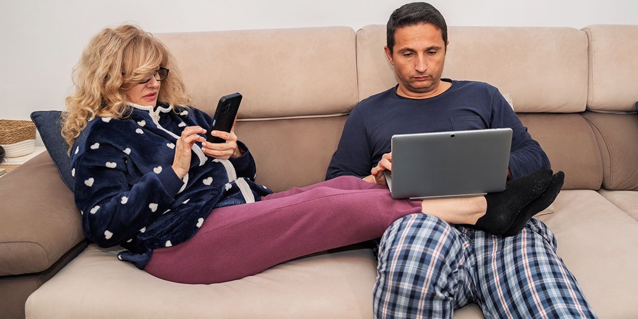 Couple on a couch, engaged with devices, contemplating love and relationships & experiencing communication issues.
