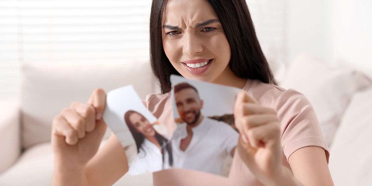 Woman distressed, tearing a photo in half, indicating betrayal.