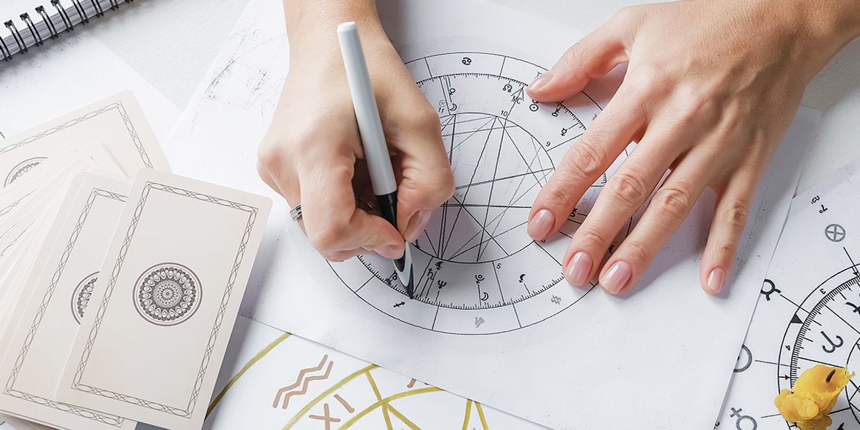 A person drawing a birth chart, showcasing astrology symbols and tools.