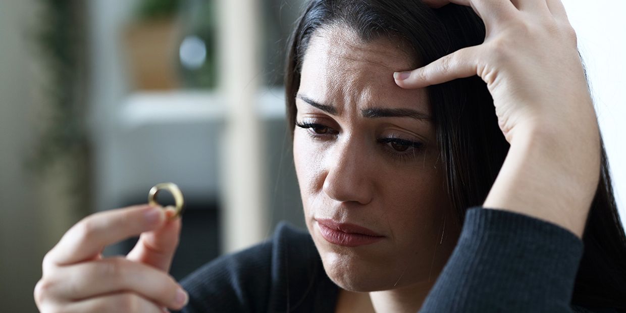 Woman reflecting on her relationship, holding a wedding ring.