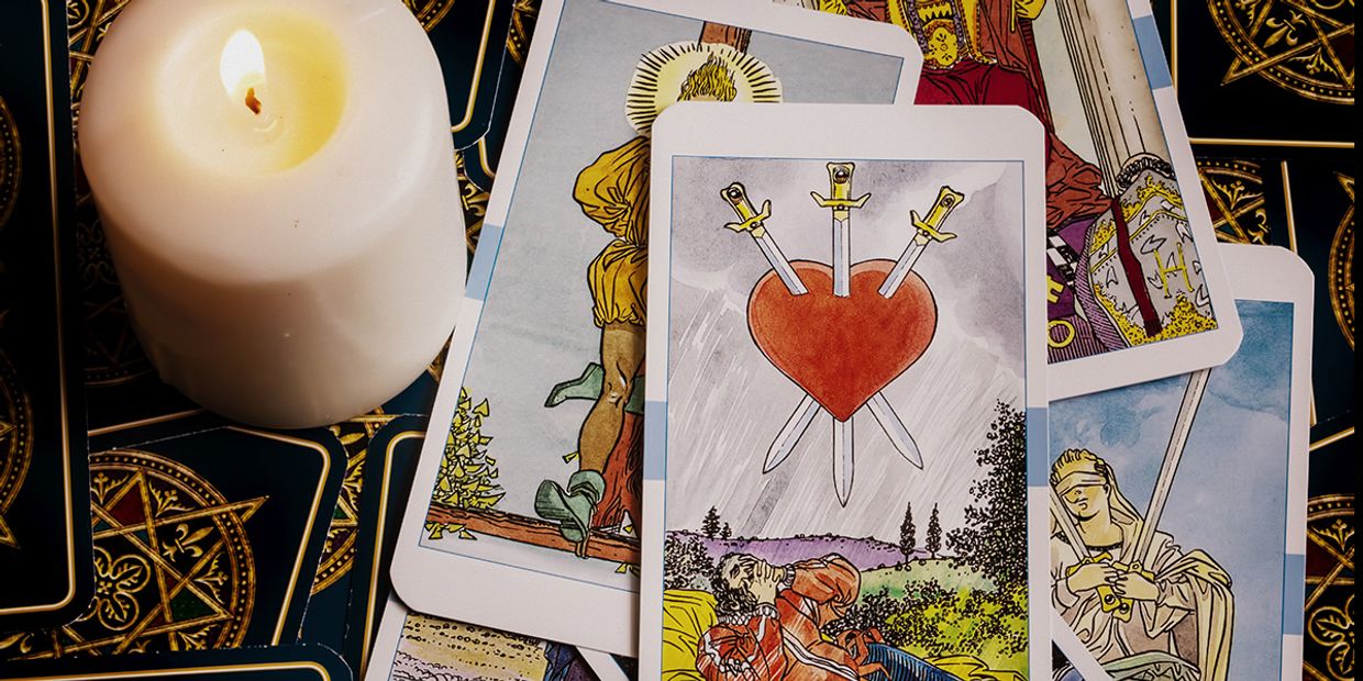 3 of hearts tarot card with a white candle nearby.
