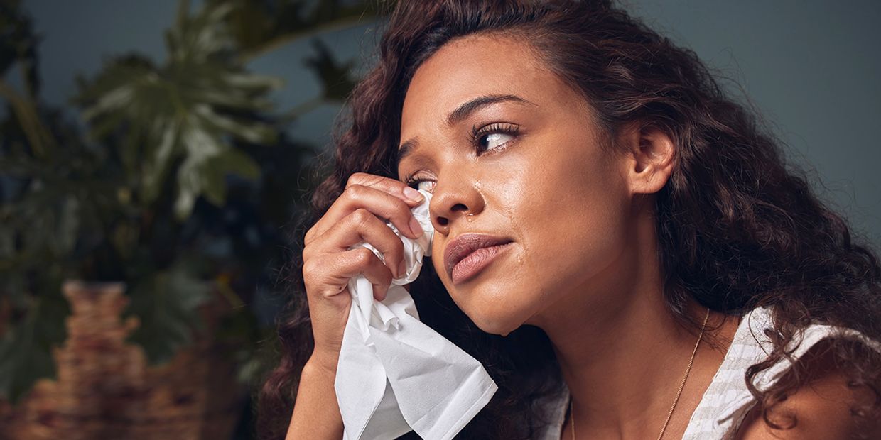 A sad and unhappy woman, wiping away her tears with a tissue.