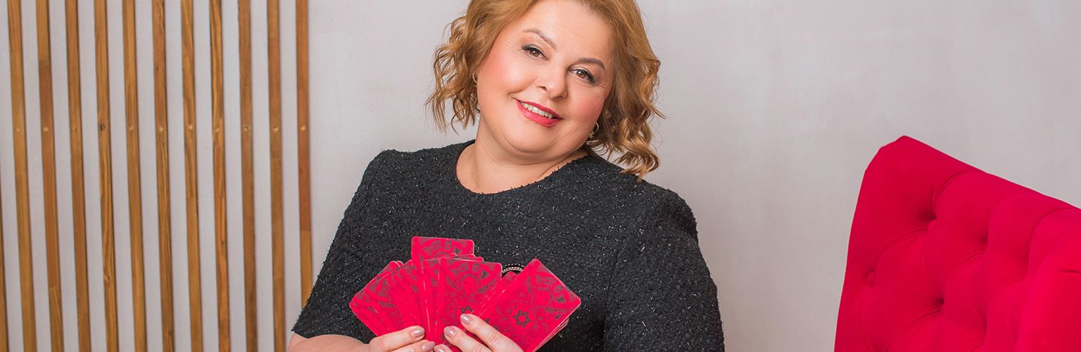 A middle aged female psychic reader, holding her tarot cards in her living room.