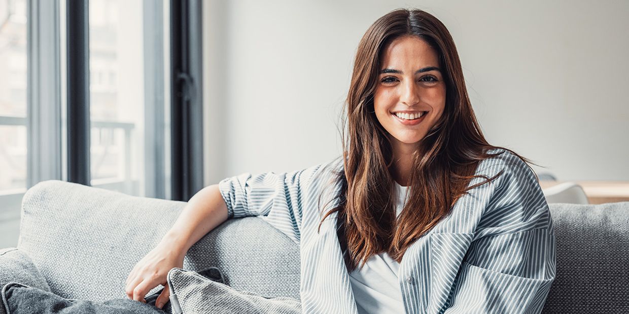 An image of a single lady in her 30's, sitting in her living room.