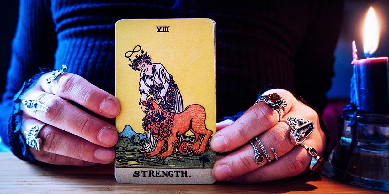 A psychic displaying the Strength tarot card next to a burning candle, representing courage, compassion, and emotional resilience.