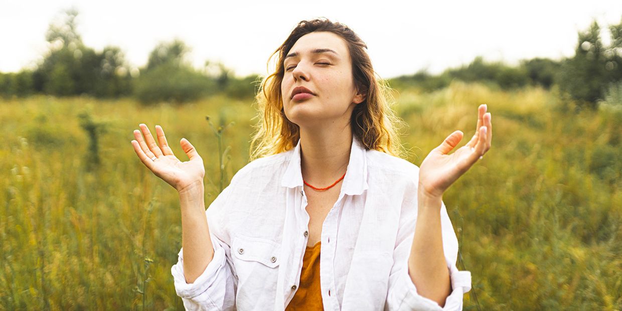 A woman seeking spiritual growth in a green field, looking up at the heavens.