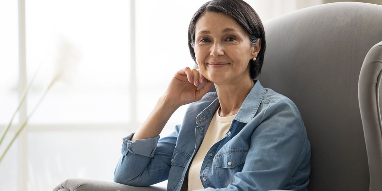 Calm middle-aged woman smiling while sitting at home, symbolising emotional healing, reassurance, and personal growth following a psychic reading.