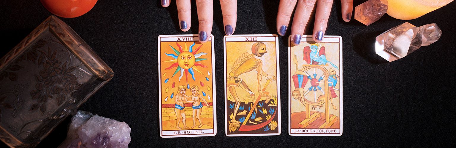 Sun, Death, and Wheel of Fortune cards spread out on a black table with crystals and candles, exploring their meanings in a three-card tarot spread.