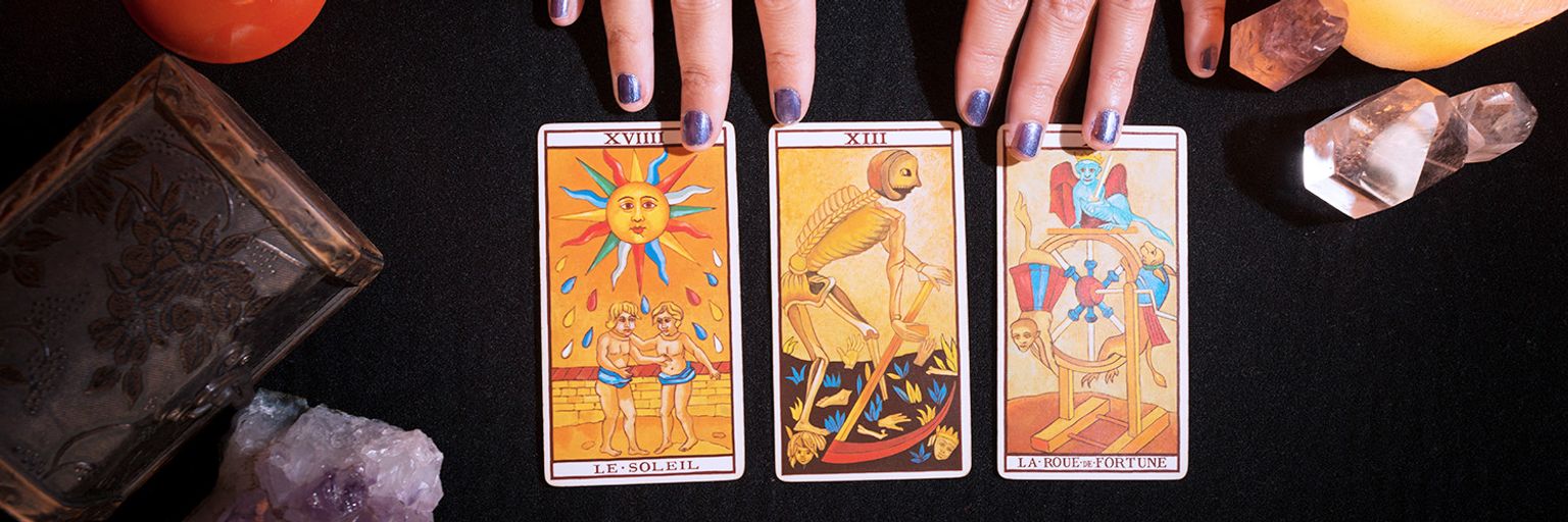Sun, Death, and Wheel of Fortune cards spread out on a black table with crystals and candles, exploring their meanings in a three-card tarot spread.