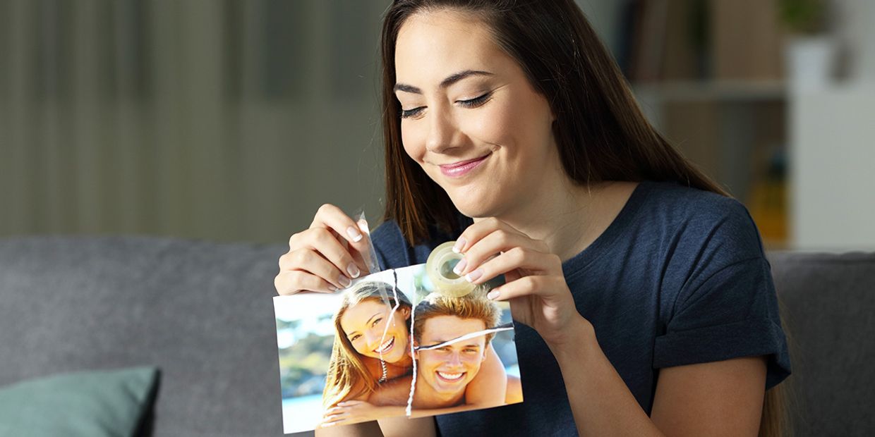 A woman sticking back together a photo of her and her boyfriend, that she ripped apart.