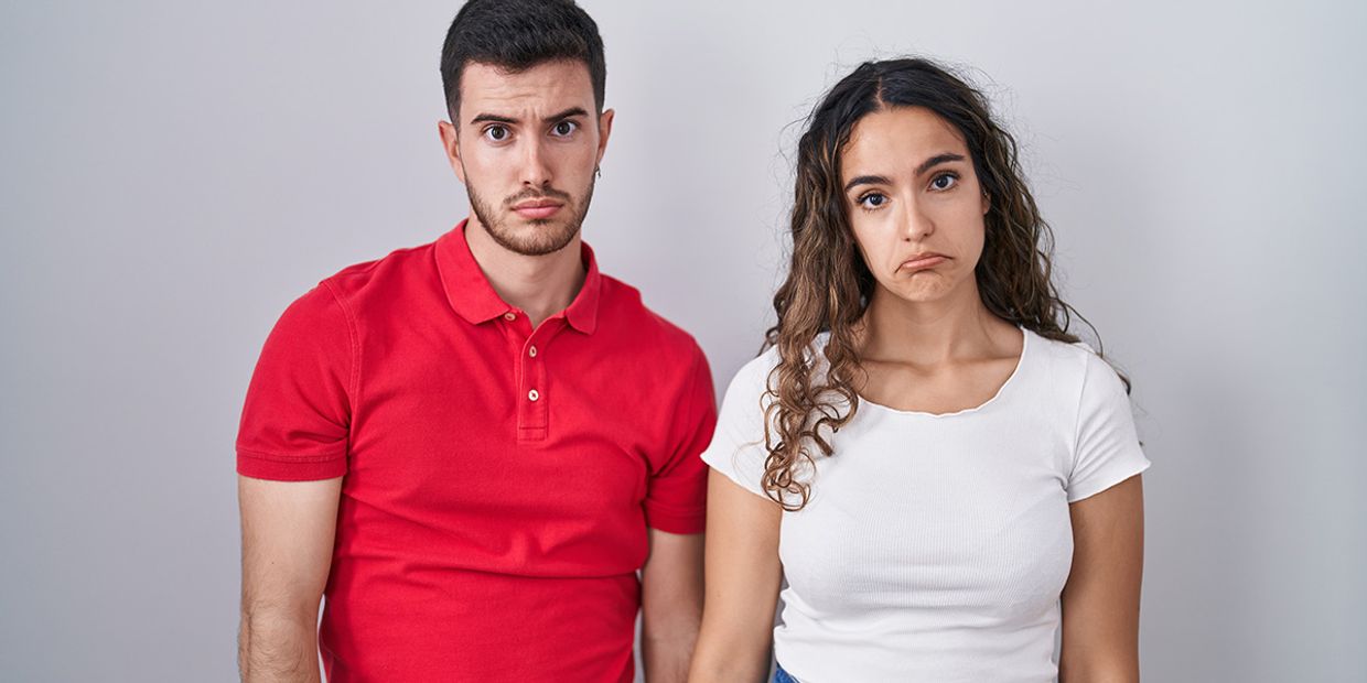 A couple looking disinterested on a plain background