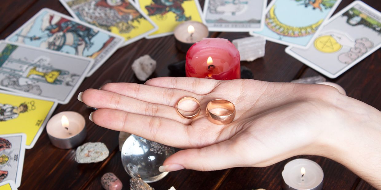 Tarot reader holding wedding rings with tarot cards and candles around them.
