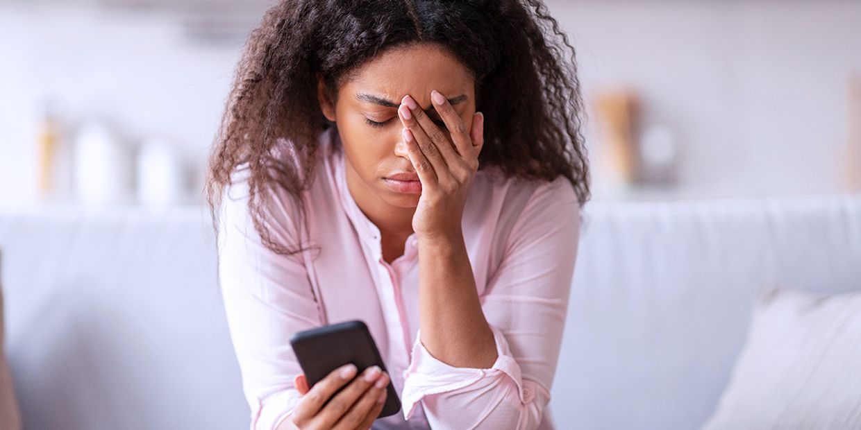 A overwhelmed woman, sitting in her living room, holding her iphone.