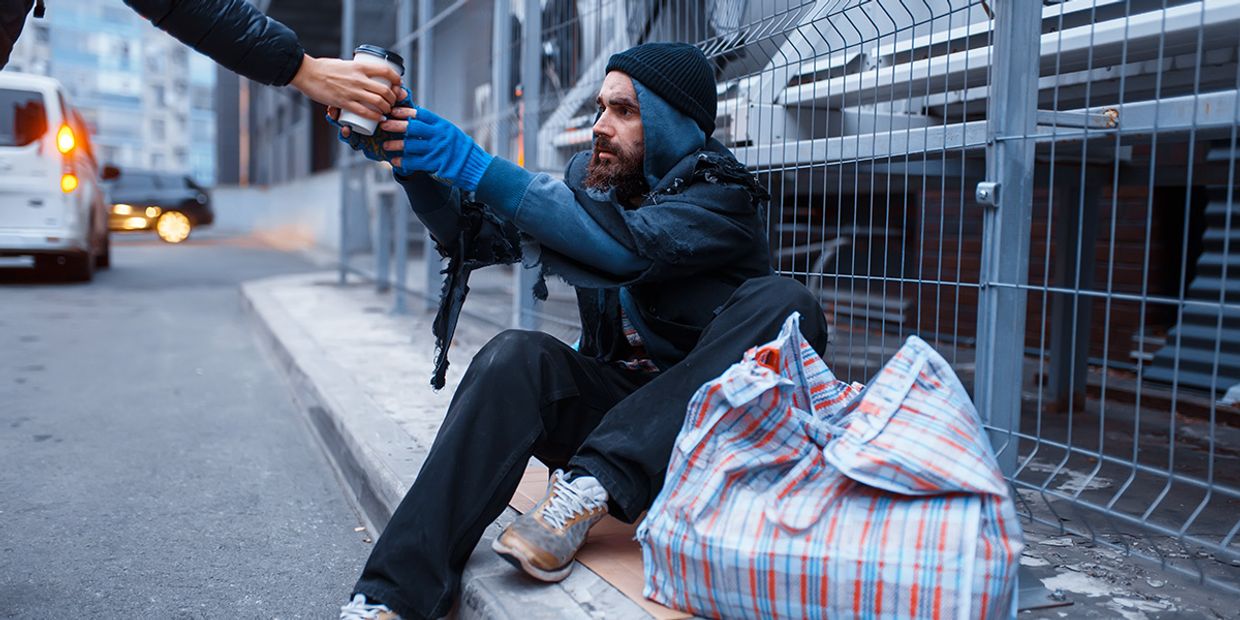 A homeless man on the street, receiving a cup of coffee.