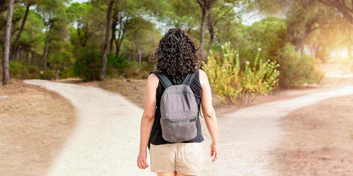 A young lady, walking in a forest, deciding which path to take.