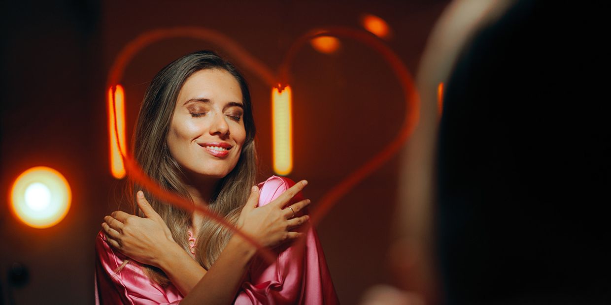 A woman hugging herself in the mirror, practicing self love.