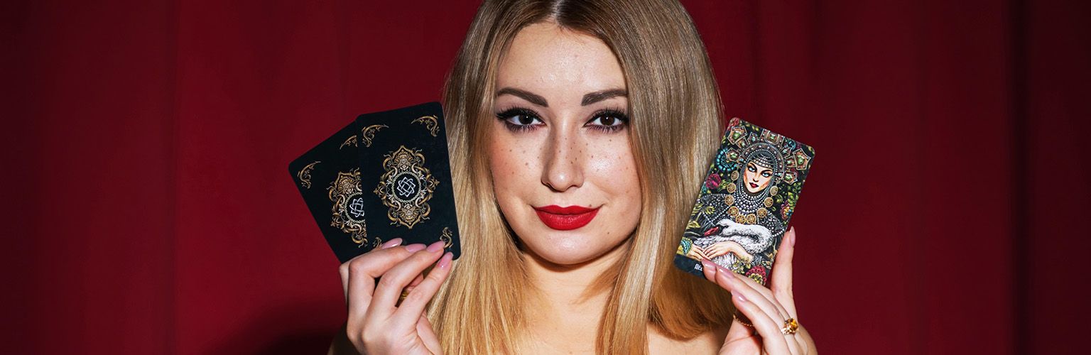 A young psychic tarot reader, holding her tarot cards to her face.