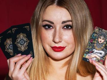 A young psychic tarot reader, holding her tarot cards to her face.