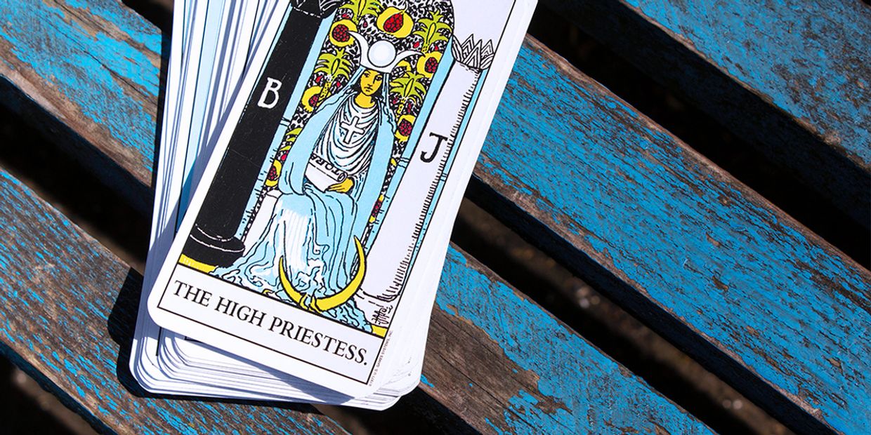 The High Priestess tarot card is on a worn blue wooden bench, representing intuition, the unknown, and spirituality.