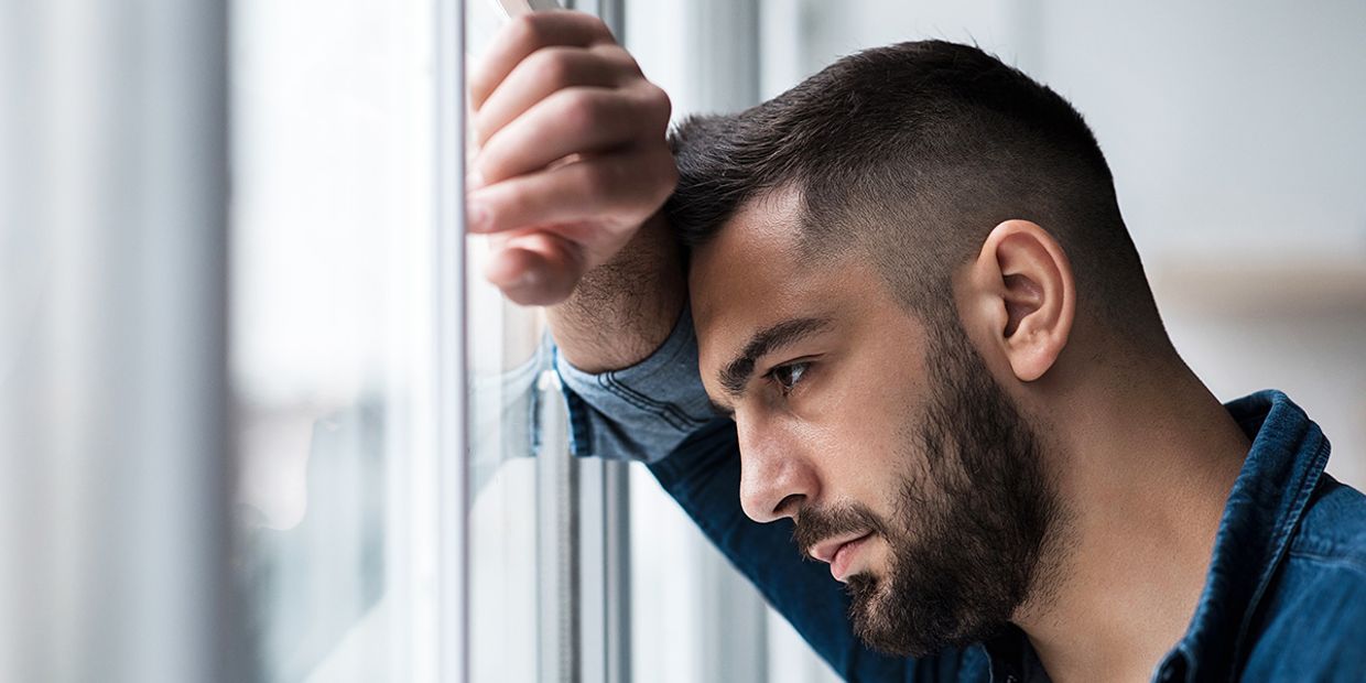 Pensive man gazing out a window, reflecting on his feelings after a breakup.