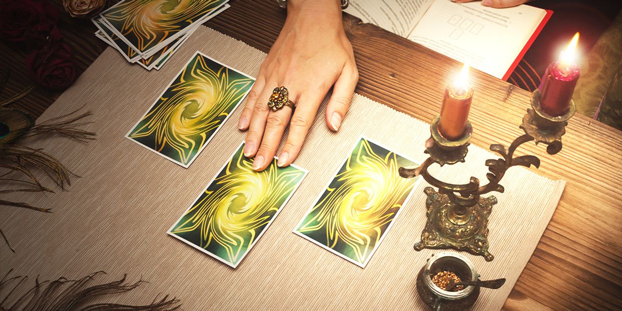 A tarot reader arranging three tarot cards on a table surrounded by candles, a ritual bowl, and peacock feathers, symbolising insight, intuition, and divination.