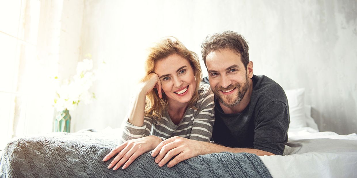 Happy couple smiles on a bed, embodying love and connection.