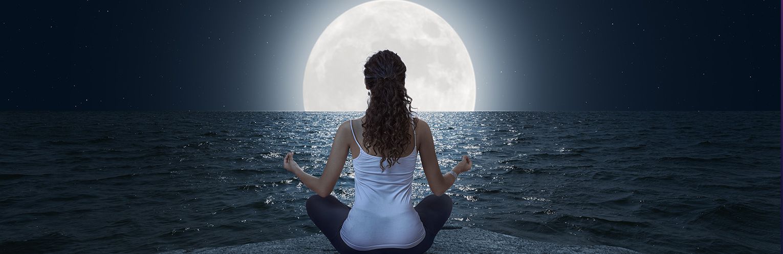 A woman meditating in front of a full moon.