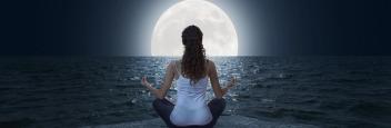 A woman meditating in front of a full moon.