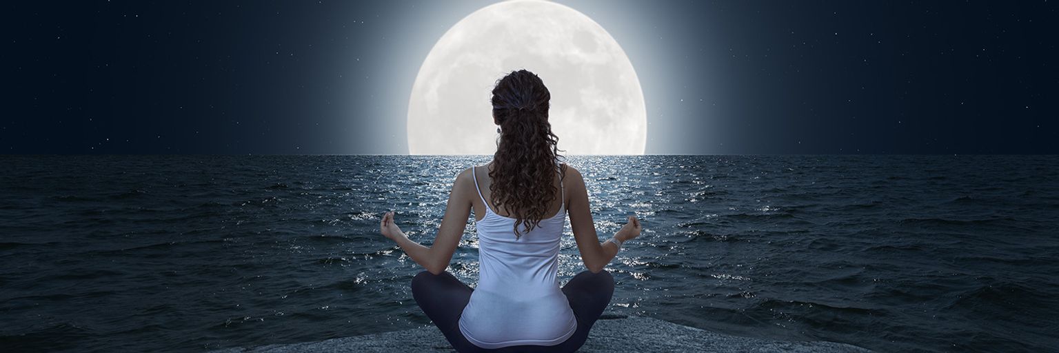 A woman meditating in front of a full moon.