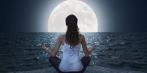 A woman meditating in front of a full moon.