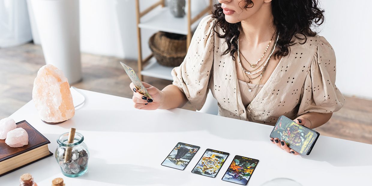 A female tarot reader, reading the tarot cards on a white desk.