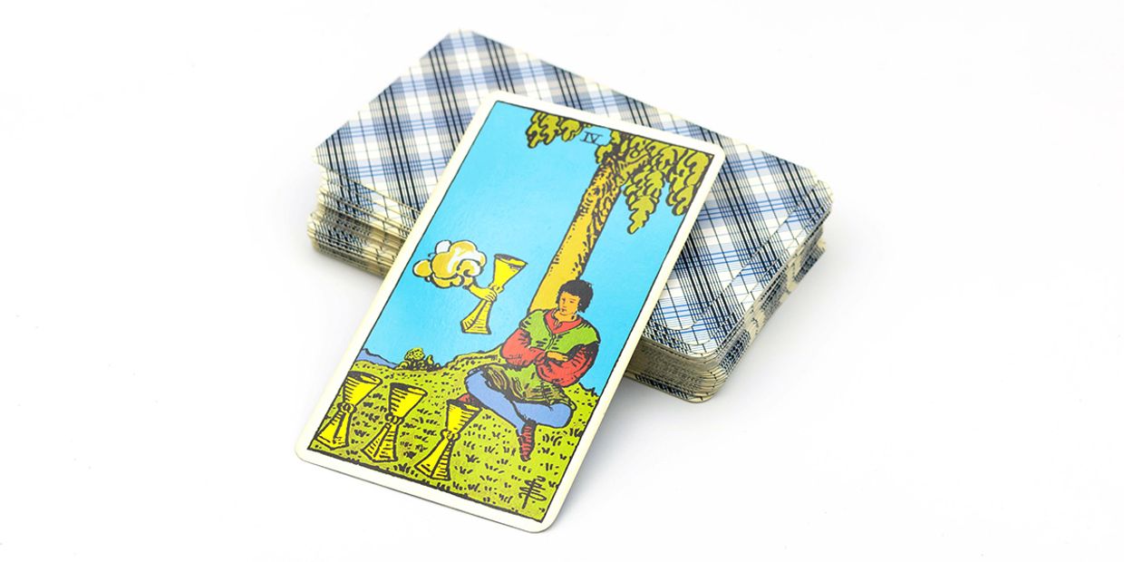 A Four of Cups tarot card resting on top of a traditional tarot deck.