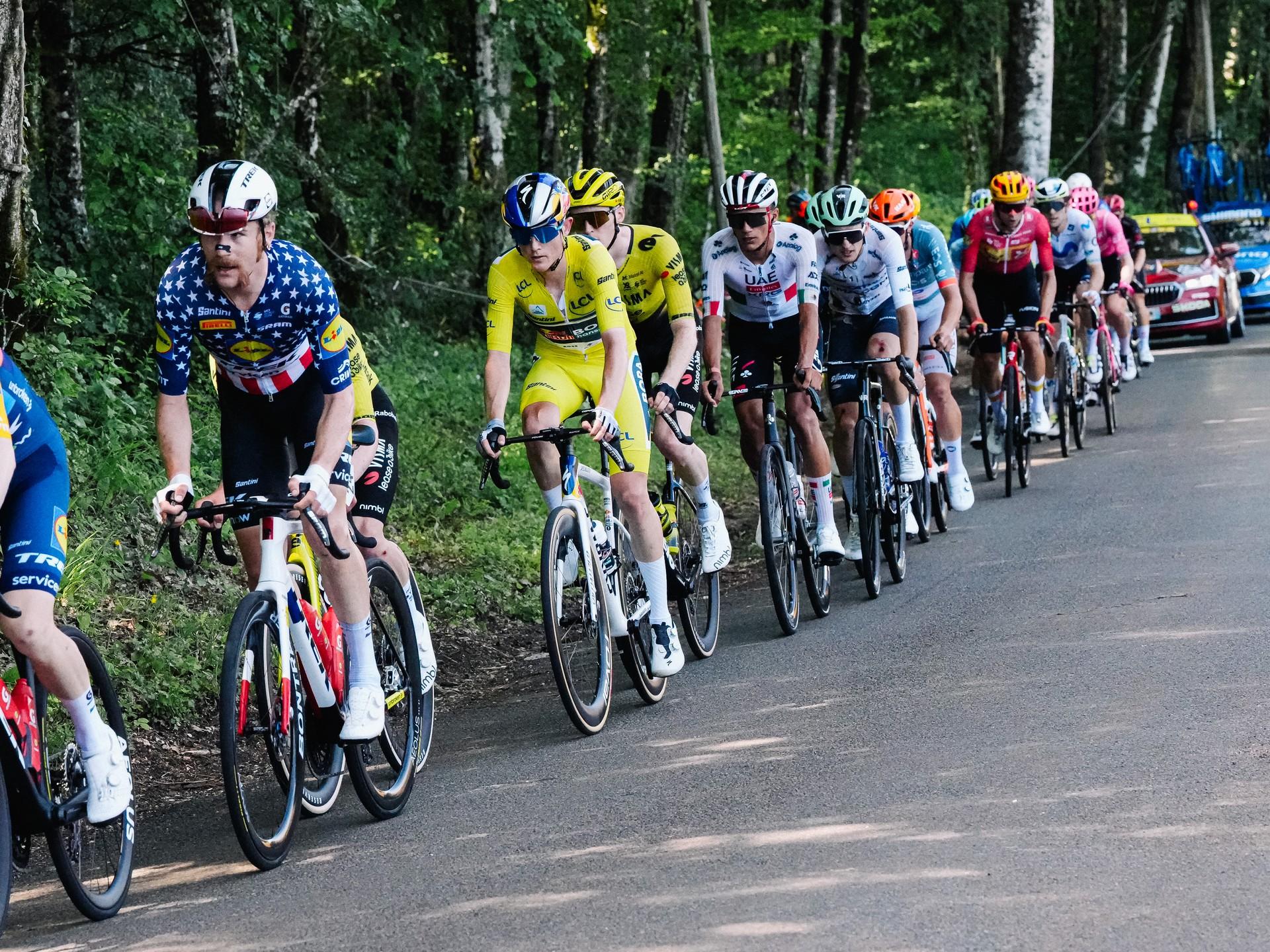 Peloton of cyclists rides single file up a mountain road during Tour Auvergne Rhône Alpes Etape 7