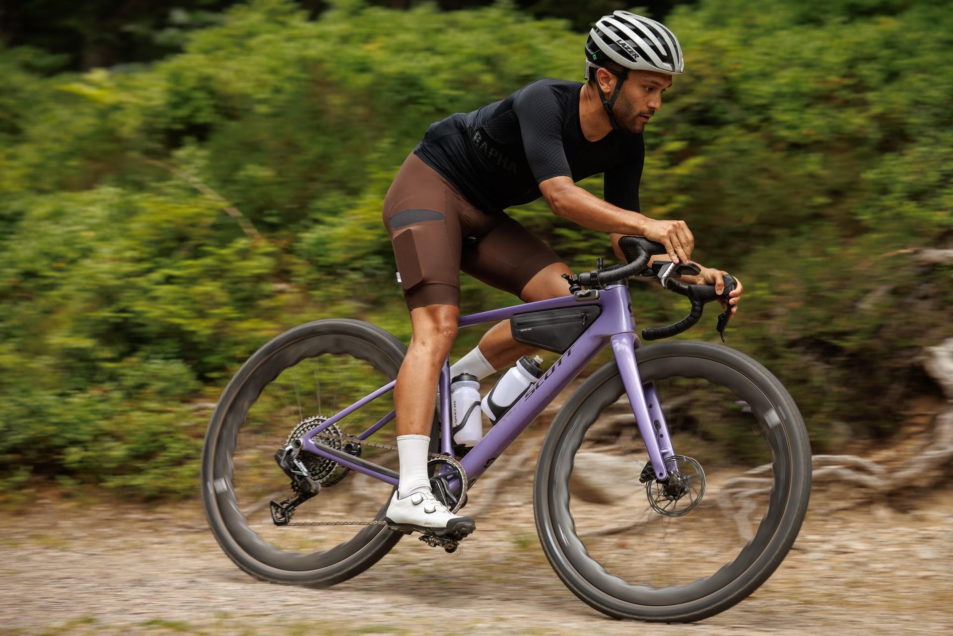 Cyclist riding a purple Scott Addict Gravel bike along a forest trail