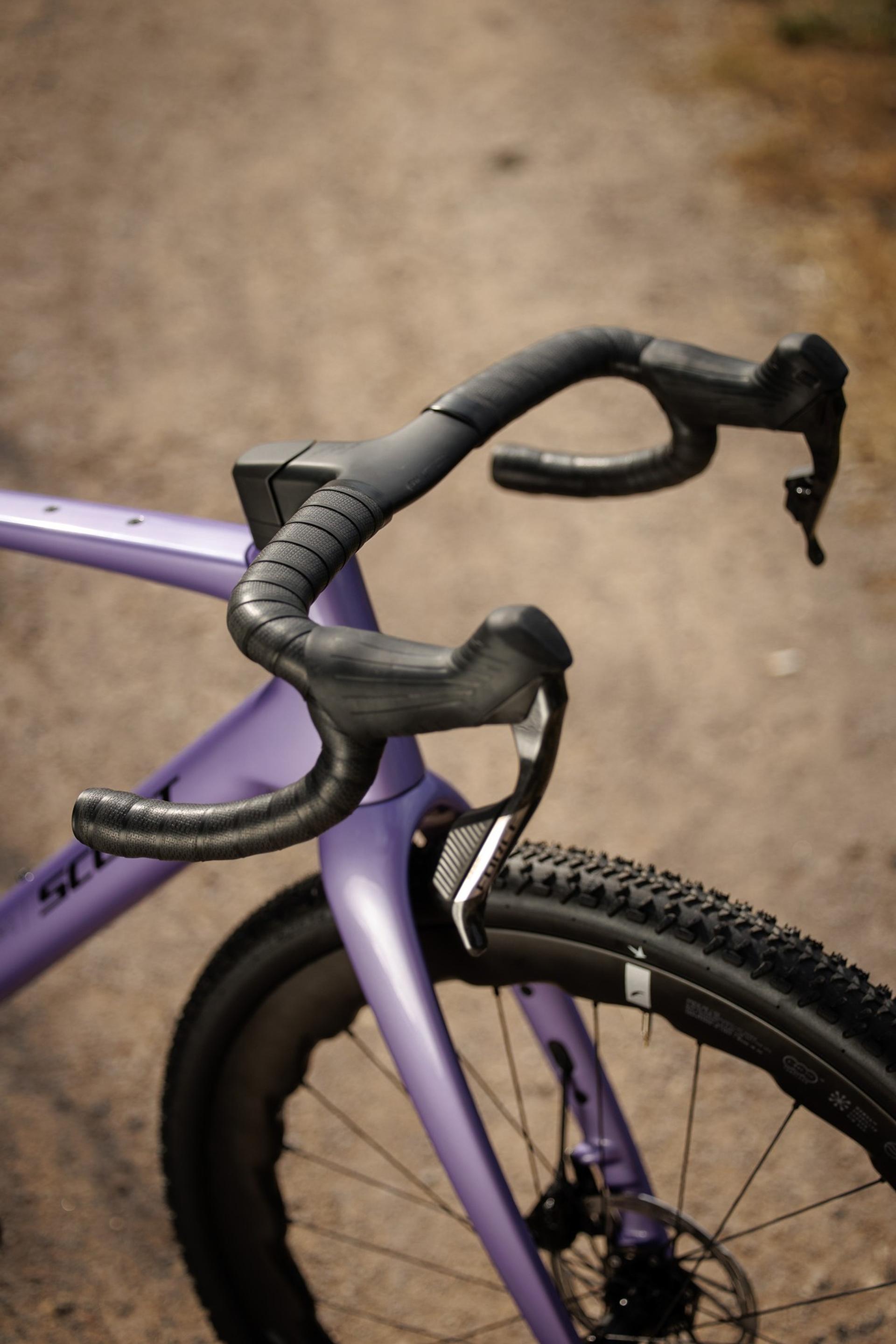 Close-up of a purple Scott Addict Gravel bike's drop handlebars, fork and knobby front tyre