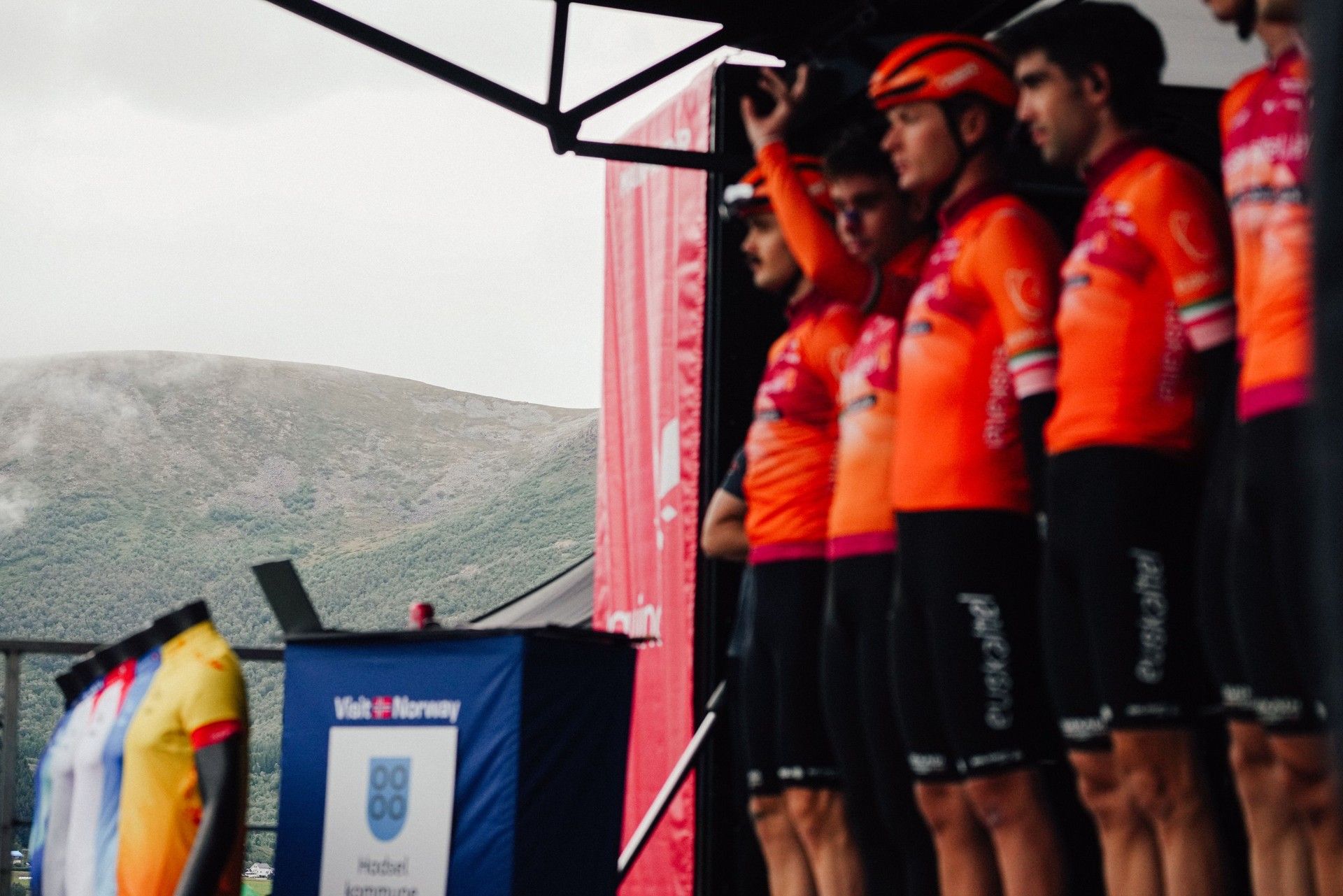 Cyclists in bright orange jerseys stand on a stage at the Arctic Race of Norway