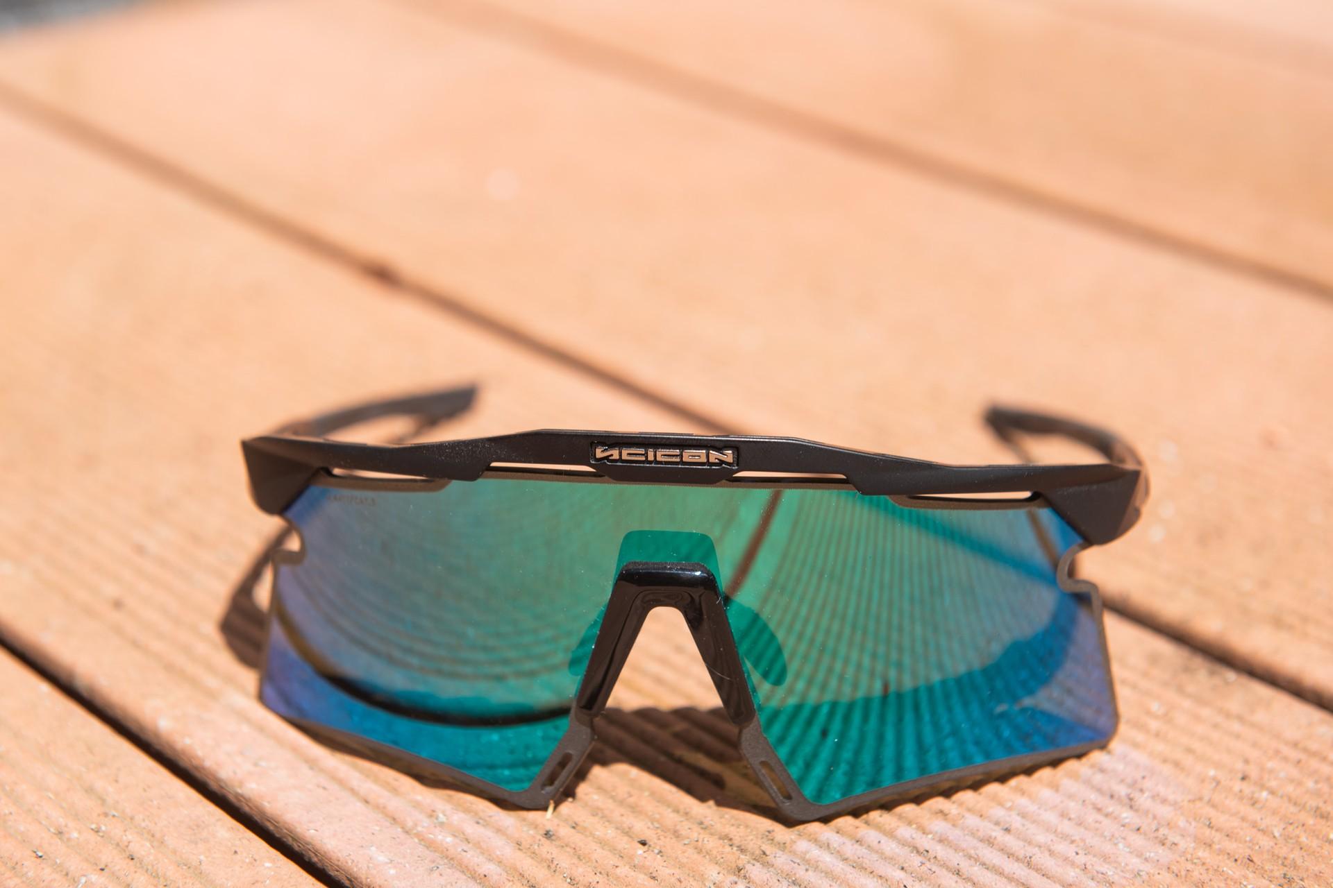 Cycling sunglasses with teal mirror lenses lying on a wooden track surface